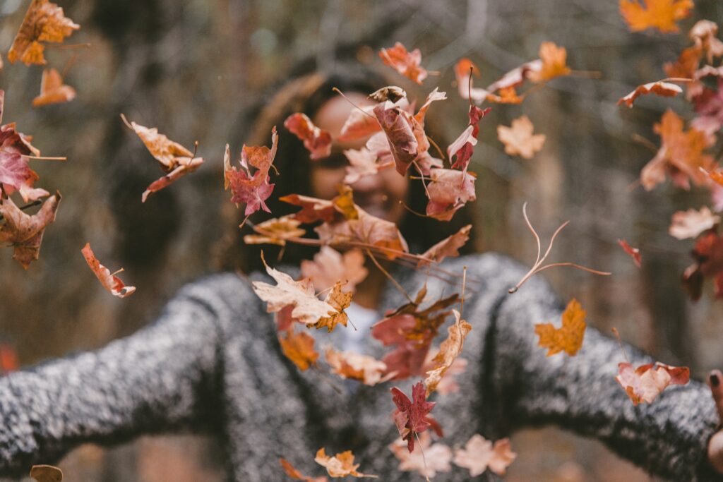 A woman throwing dried leaves up in the air.